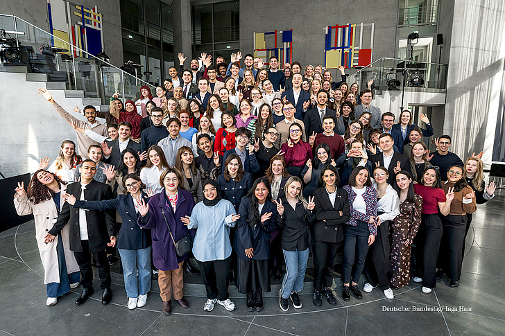 IPS-Stipendiaten Eine große Gruppe junger Menschen posiert lächelnd in einem modernen Gebäude mit farbigen Kunstwerken an der Wand.